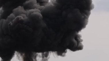 Yoğun siyah duman yükseliyor, soluk gökyüzüne karşı dramatik ve yoğun bir atmosfer yaratıyor.