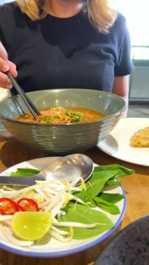 İyi aydınlatılmış Bangkok restoranında taze malzemelerle Vietnam piposunun tadını çıkaran bir insan, mutfak zevkini ve kültürel birleşimi ön plana çıkarıyor.