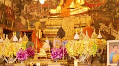 Wat Arun, Bangkok 'ta dingin altın bir Buda heykeli, canlı çiçekler ve sıcak ışık altında süslü süslemelerle çevrili.