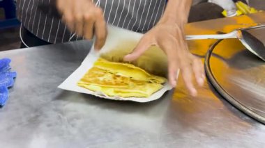 Bir sokak satıcısı, Tayland 'ın Phuket şehrinde geleneksel sokak yiyeceklerini sergileyerek, metal bir yüzey üzerinde ustaca Tayland roti doğruyor.