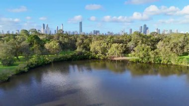 İnsansız hava aracı, Avustralya 'nın Gold Coast şehrinde gün ışığında yemyeşil parkı ve şehrin ufuk çizgisini yakalar. Canlı yeşillik ve yansıtıcı su