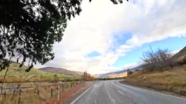 Wanaka, Yeni Zelanda 'da dolambaçlı bir yol boyunca sakin bir sürüş dramatik bir gökyüzü altında sonbahar yapraklarını sergiliyor.