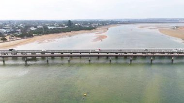 Hava görüntüleri, Barwon Heads köprüsünden geçen bir aracı gün ışığında sakin bir nehrin üzerinden yakalıyor.