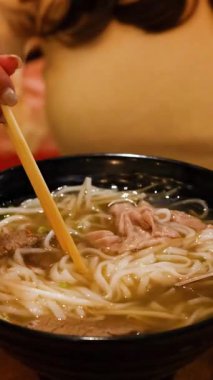 Bir insan sıcak bir ortamda Vietnam piposunun tadını çıkarmak için çubuk kullanır, yemeğin zengin dokularını ve lezzetlerini ön plana çıkarır.