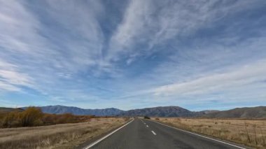 Queenstown, Yeni Zelanda kırsal bir yolda sakin bir sürüş, yumuşak gün ışığı altında geniş gökyüzü ve sonbahar yaprakları sergileniyor