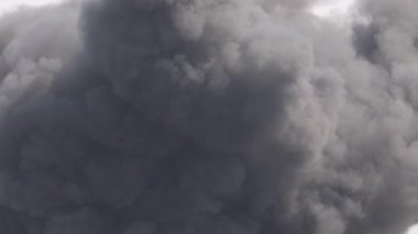 Yoğun, koyu duman bulutları yoğun bir şekilde dalgalanıyor. Çerçeveyi dinamik hareketler ve dramatik atmosferle dolduruyor.