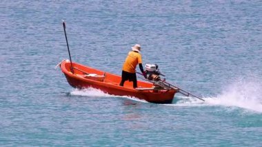 Balıkçı, Phuket 'teki okyanus sularını hızla geçen uzun kuyruklu bir tekneyi sürüyor.