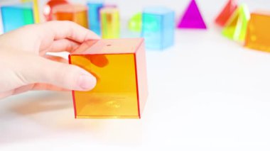 Eller beyaz bir yüzey üzerinde renkli şeffaf küpleri manipüle ederek, geometrik kavramları canlı ışık ve net odak ile çizer