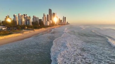 Güneş doğarken Altın Sahil 'in havadan görünüşü, okyanus dalgalarını ve şehir siluetini yakalıyor, sıcak, altın bir ışık altında.