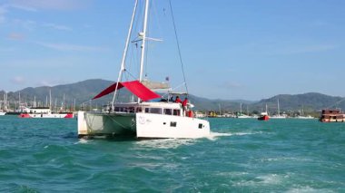 Phuket, Tayland 'da berrak gökyüzünün altında, canlı mavi sularda yelken açan kırmızı bir yat.