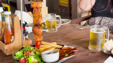 Tayland, Phuket 'te bir sahil kulübünde şiş, patates kızartması ve birayla sıradan bir yemek sahnesi. Parlak, rahat bir atmosfer.