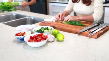 İki kişi mutfak tezgahında taze sebze ve otlar hazırlıyor. Parlak ışıklandırma ve temiz, modern estetik...