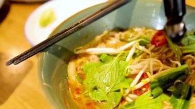 Bir Bangkok restoranında sıcak bir ışıkta yakalanan canlı bir kase Vietnam pilavı taze otlar ve sosla süslenir.