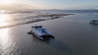 Gün batımında marina yakınlarında seyreden bir katamaranın havadan çekilmiş görüntüleri dingin suları ve altın saati aydınlatıyor.