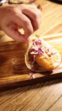 Elleri ahşap bir tahtanın üzerinde lahanalı bir balıklı taco hazırlıyor.