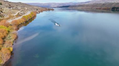 Güz yaprakları ve dağlarla çevrili, temiz gökyüzünün altında, Dunstan Gölü 'nde uçan bir jet ski manzarası.