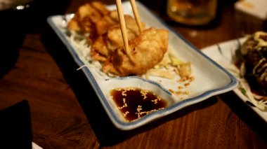 Yemek çubukları bir sos tabağından gyoza kaldırıyor.