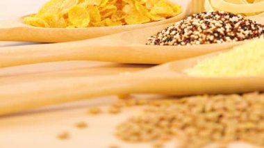 Kinoa, mercimek, kuskus ve tahta kaşıklarda mısır gevreği yakın çekim. Ilık ışıklandırma dokuyu ve renk karşıtlığını artırır