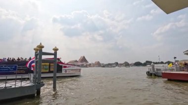 Chao Phraya nehri boyunca bulutlu bir gökyüzünün altında yüzen bir nehir teknesi Bangkok 'un canlı atmosferini yakalıyor.