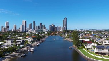 İnsansız hava aracı görüntüleri, açık mavi gökyüzünün altında Altın Sahil 'in ufuk çizgisini ve su yollarını yakalıyor. Şehir mimarisi ve doğal güzellikleri gözler önüne seriyor.