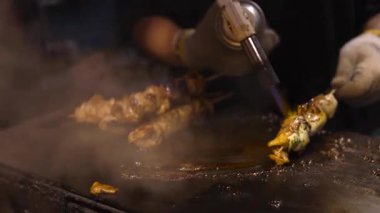 Şef meşaleyle şişe geçirilmiş et pişiriyor.