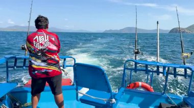Tayland, Phuket 'te bir tekneden bir insan balık avlar. Parlak gün ışığında dalgalı okyanus sularında yol alır.