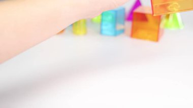 Eller, beyaz bir yüzeyde yarı saydam geometrik şekilleri manipüle eder. Parlak renkler ve eğlenceli düzenleme eğitici ve çekici bir atmosfer yaratır