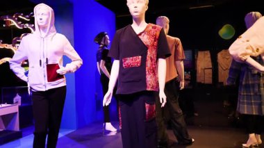 Mankenler, dinamik ışıklandırma ve koyu renklerle modern bir galeri ortamında canlı, seçici bir moda sergilerler.