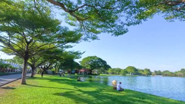 Bangkok 'taki Rama IX Parkı' nda, açık mavi gökyüzü ve yemyeşil bir havuzun altında dinlenen bir insanın sakin bir görüntüsü.