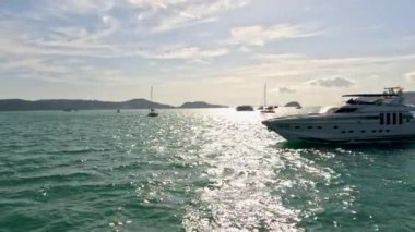 Phuket, Tayland yakınlarındaki ışıl ışıl sularda süzülen lüks bir yat, berrak bir gökyüzünün altında, huzurlu sahil güzelliğini yakalıyor.