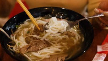 Bir insan sıcak bir ortamda yemek çubukları ve kaşıkla bir kase Vietnamlıların tadını çıkarıyor.