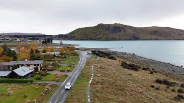 Tekapo Gölü 'nün yanındaki sarmal bir yolun havadan görünüşü sonbahar yapraklarını ve bulutlu gökyüzünün altındaki sakin suları gösteriyor.