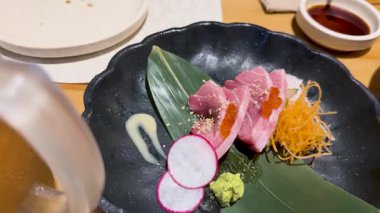 Toro ton balıklı sashimi 'ye yakın çekim. Siyah bir tabakta, wasabi ve turpla. Parlak ışık altında.