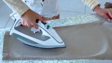 İyi ışıklandırılmış bir odadaki panodaki pantolonları ütüler, düzgün, hassas hareketlere odaklanır.