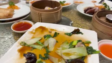 Dönüşümlü bir tablo çeşitli Dim sum yemekleri gösterir, bunlar arasında börekler, sebzeler ve soslar, parlak bir ortamda