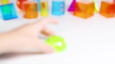 Bir el, eğitici oyun ve dokunsal keşifleri vurgulayarak, beyaz bir yüzeyde canlı üç boyutlu geometrik şekilleri manipüle eder.