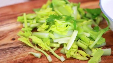 Ahşap bir tahtaya doğranmış kereviz yerleştiren ve parlak ışığın altında bir kaseye yerleştiren eller.