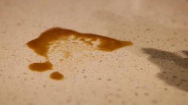 Sıcak ışık altında sarı bir bez kullanarak benekli bir tezgahın üzerine kahve dökülmesini temizleyen bir insan.