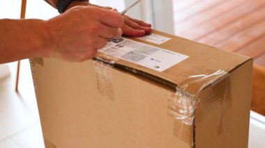 Eller dikkatlice kapalı bir karton kutuyu iyi aydınlatılmış bir odada bıçak kullanarak açar.