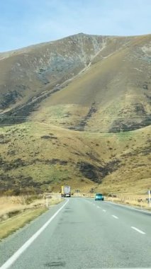 Tekapo Gölü 'nün göz kamaştırıcı dağlık arazisiyle çevrili dolambaçlı bir yolda bir araç seyahat ediyor.