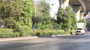 Beyaz teslimat kamyonu ağaçlık bir caddede ilerliyor.