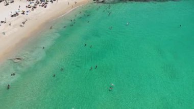 Drone görüntülerinde canlı bir Phuket plajında turkuaz sular ve kumlu sahillerde güneşli bir günün tadını çıkaran turistler görülüyor.