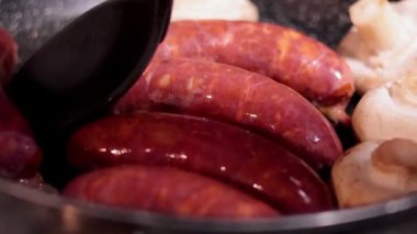 Tavada pişen sosis ve mantarlar.