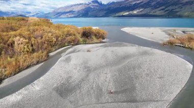 İnsansız hava aracı görüntüleri, berrak gökyüzünün altında dalgalı sonbahar yapraklarının arasından süzülen sakin bir nehri yakalıyor. Doğal güzellik ve sakinlik sergiliyor.