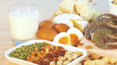 Fındık, yumurta ve süt ürünleri de dahil olmak üzere çeşitli protein zengini yiyecekler mavi arka planda doğal ışıklandırmayla sergilenmektedir.