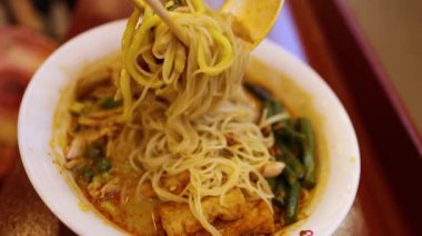 Yemek çubuğu ve kaşıkla erişte çorbası içen kişi.