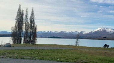 Turistler, açık gökyüzünün altındaki dağlar ve ağaçlarla çevrili Tekapo Gölü 'nün sakin manzarasının tadını çıkarıyorlar.