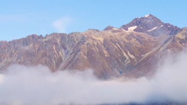 Dağ zirveleri açık mavi bir gökyüzünün altında yuvarlanan sis yüzünden kısmen gizleniyor. Glenorchy, Yeni Zelanda 'da Yakalandı