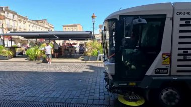 Sokak temizleyicisi hareketli bir kafenin önünden geçiyor.