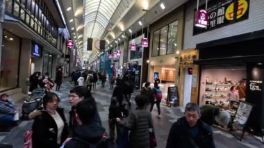 Kalabalık bir alışveriş caddesinde yürüyen insanlar